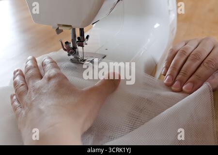 close up view of sewing process. Female hands stritching white fabric Stock Photo