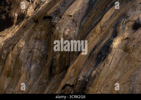 Striated Rock Formation: Golden-Brown Hues with Dark Streaks and Geological Texture Stock Photo