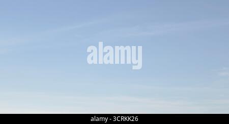 Clean soft pale blue sky with very faint almost imperceptible wisps cirrus clouds. Sky smooth gradient shifting from slightly lighter shade bottom pas Stock Photo