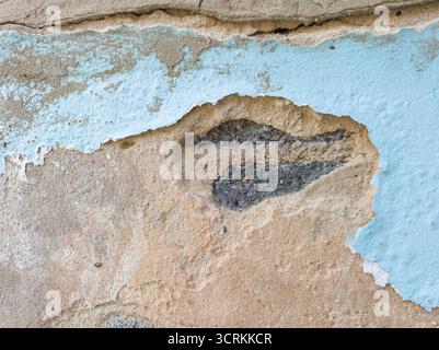 Close-up severely damaged and peeling light blue wall, revealing a large hole in the plaster exposing the concrete underneath. Focusing on the layers Stock Photo