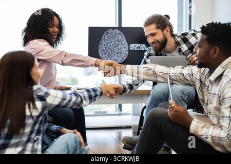 Diverse team celebrates success with a handshake in a tech environment Stock Photo