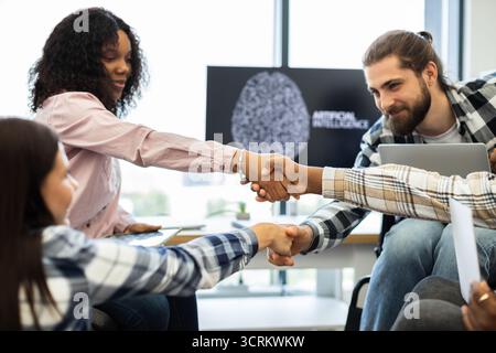 Diverse team celebrates success with a handshake in a tech environment Stock Photo