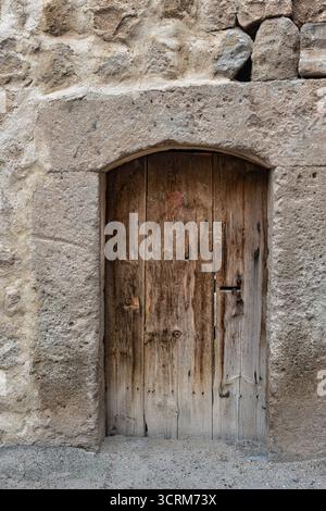 Weathered wooden door with an arched stone frame set into a rustic stone wall. Features aged wood texture, cracks, and rusty details. Vertical shot Stock Photo