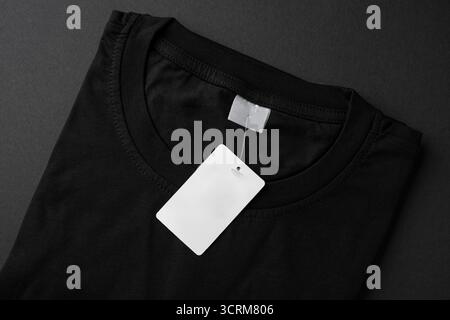 Folded black t-shirt with blank paper tag on dark background Stock Photo