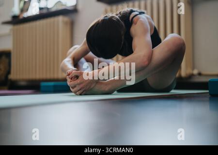 Woman Practicing Advanced Stretch on Yoga Mat During Indoor Workout Session Stock Photo