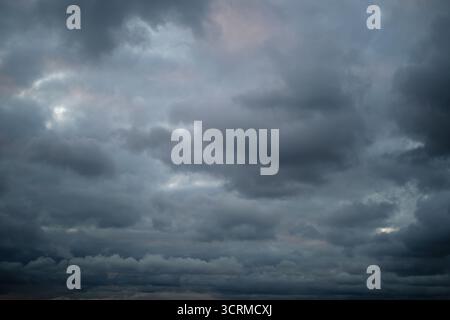 Dramatic dark clouds gather in the sky, creating a moody and stormy atmosphere with shades of gray and hints of fading light. Stock Photo
