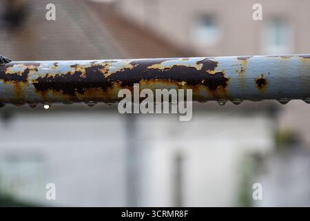 Close-up macro image of raindrops on rusted gray metal railing with artistic soft-focus background of rainy scenery. Stock Photo