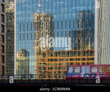Reflections on a glass building DLR train on bridge warn colours Stock Photo