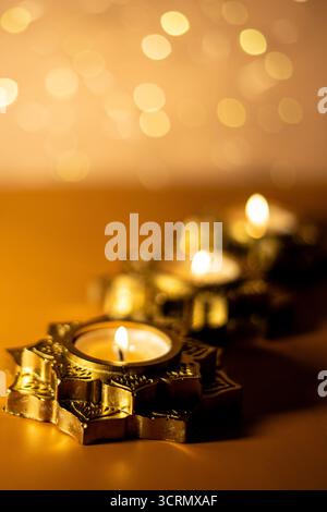 A close-up photograph of a glowing candles placed in a beautifully ornate, star-shaped golden holder. Selective focus. Stock Photo