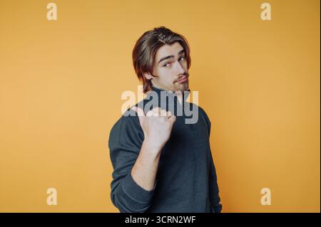 Young man giving a thumbs up in front of a bright yellow background during casual indoor portrait session Stock Photo