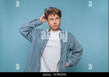 A young man stands with a contemplative expression, wearing a denim jacket over a white shirt. He appears to be lost in thought, combining casual styl Stock Photo