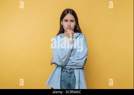 Young woman in casual attire pouting against a yellow background. Stock Photo