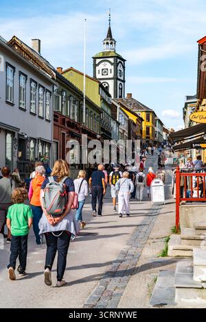 Tourists walk along the charming shopping street of Røros, Norway, taking in the historic buildings and vibrant atmosphere on a pleasant summer day. Stock Photo