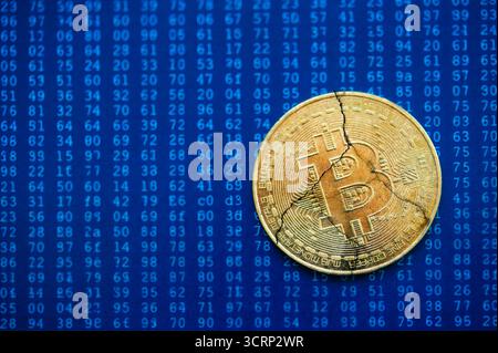 Cracked golden Bitcoin coin on binary code background symbolizing cryptocurrency crash or market instability Stock Photo