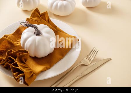 Autumn and Thanksgiving day table setting with plate decorated white pumpkins on beige table. Close up. Stock Photo