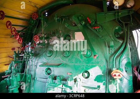 Inside a historical steam engine, the vibrant green control panel displays an array of valves and instruments. Sunlight highlights the detailed machin Stock Photo