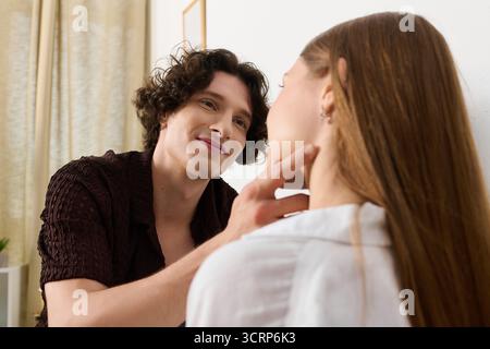 A smiling young man touches the cheek of a beautiful woman in their modern apartment. Stock Photo