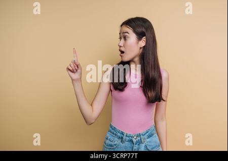 Young woman in pink top and jeans pointing with surprise Stock Photo