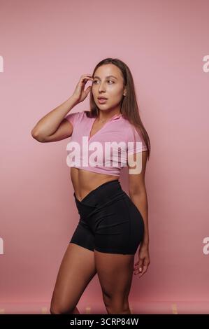 Woman in athletic wear posing against a pink background. Stock Photo