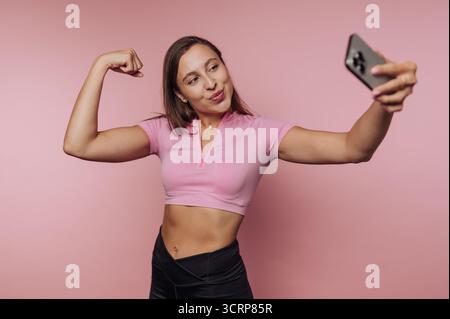 Woman in pink top taking a selfie while flexing her arm. Stock Photo