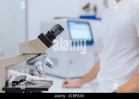 A scientist in a white shirt analyzes samples through a microscope in a modern laboratory setting. Stock Photo