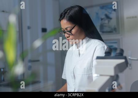 Female laboratory technician pipetting blood sample on the slide, preparing specimen for microscope examination. Blood testing concept. Stock Photo