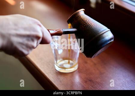 A transparent glass cup with coffee remnants sits on a wooden windowsill. The scene suggests a finished drink and cozy lifestyle atmosphere. Stock Photo