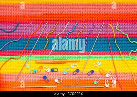 All for hand knitting. Knitted multi-colored handmade fabric with balls of multi-colored threads, pins and various knitting needles on it. Stock Photo