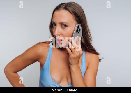 A young woman stands confidently while talking on her smartphone. She wears a light blue top, and her hair falls casually around her shoulders. The ba Stock Photo