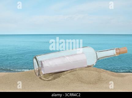 Corked bottle with rolled letter inside on sand near sea Stock Photo