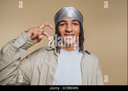 A young man is smiling and making a playful hand gesture while wearing a silver headscarf and a light-colored shirt. The simple background emphasizes Stock Photo