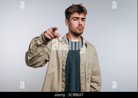 A young man stands in a studio, dressed in a casual outfit. He has a confident expression while pointing towards the camera, creating an engaging mome Stock Photo