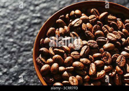 Roasted coffee beans in wooden bowl on dark background. Aromatic coffee closeup texture. Natural caffeine ingredient for hot drinks preparation. Stock Photo
