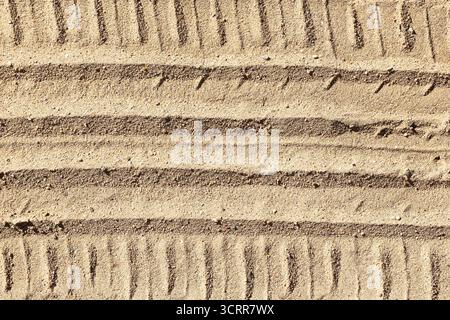 Tire tracks on sand surface. Offroad vehicle marks creating linear texture pattern. Outdoor travel and adventure background. Natural sandy ground. Stock Photo