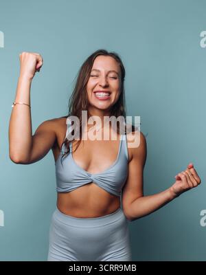 Smiling woman in athletic wear celebrating with clenched fists. Stock Photo