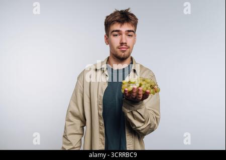 Young man holding a bunch of green grapes against a plain background. Stock Photo