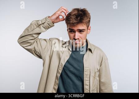 Young man scratching his head, looking confused. Stock Photo