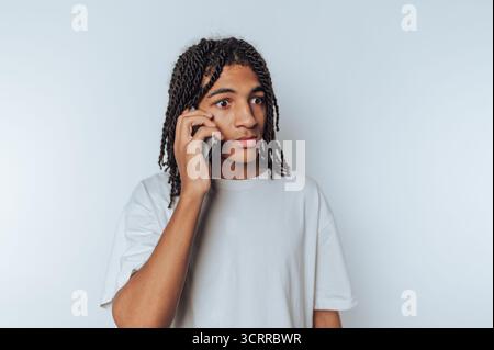 Young man with dreadlocks talking on a smartphone against a white background. Stock Photo