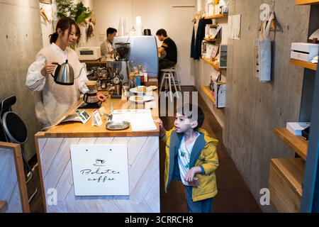 TOKYO, JAPAN - 28 OCTOBER, 2024 - Horizontal picture of a japanese woman preparing pour over coffee smilling to a boy in a coffee shop located in Toky Stock Photo