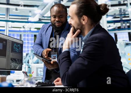 Diverse team of engineering experts discuss workflow strategy and analyzing data in a solar energy factory, reflecting shared responsibility in clean technology and innovation. Stock Photo