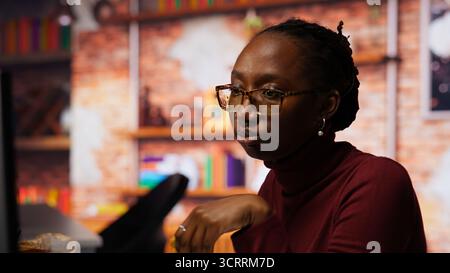 Programmer coding AI algorithm in startup, eating food at desk while refining machine learning models. Stressed woman using coding platform in Silicon Valley office and enjoying snack, camera B Stock Photo
