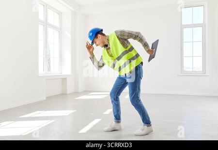 Male funny foreman wearing yellow vest and hardhat standing on building site. Stock Photo