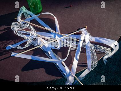 Wedding wands with white satin and lace ribbons on a table outdoors, festive detail for celebration and ceremony. Stock Photo