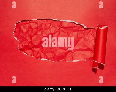 Red paper background with a torn section revealing a wrinkled texture beneath Stock Photo