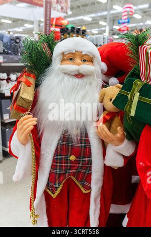 A decorative Santa Claus figurine stands in a store, holding a teddy bear and a gift, surrounded by other Christmas decor. Stock Photo
