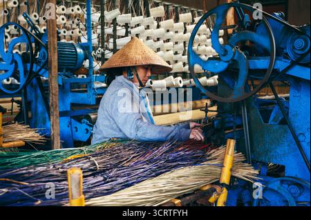 Vietnamese female weaver works on loom in a workshop at a factory producing traditional woven reed mats in Vietnam. An Cu, Tuy An, Phu Yen province, Vietnam - April 14, 2025 Stock Photo