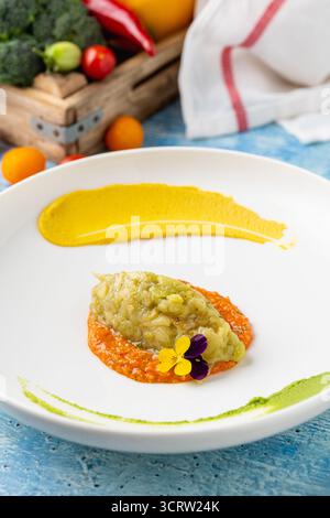 Eggplant puree with colorful sauces and edible flower garnish Stock Photo