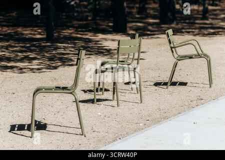 Iconic green metal chairs stand empty on a sunlit gravel path in the famous city park - Luxembourg Garden, Paris, France Stock Photo