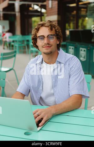 Man working on laptop at cafe, looking confidently ahead. Stock Photo
