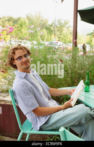 Young man reads book at outdoor cafe on a calm sunny day Stock Photo
